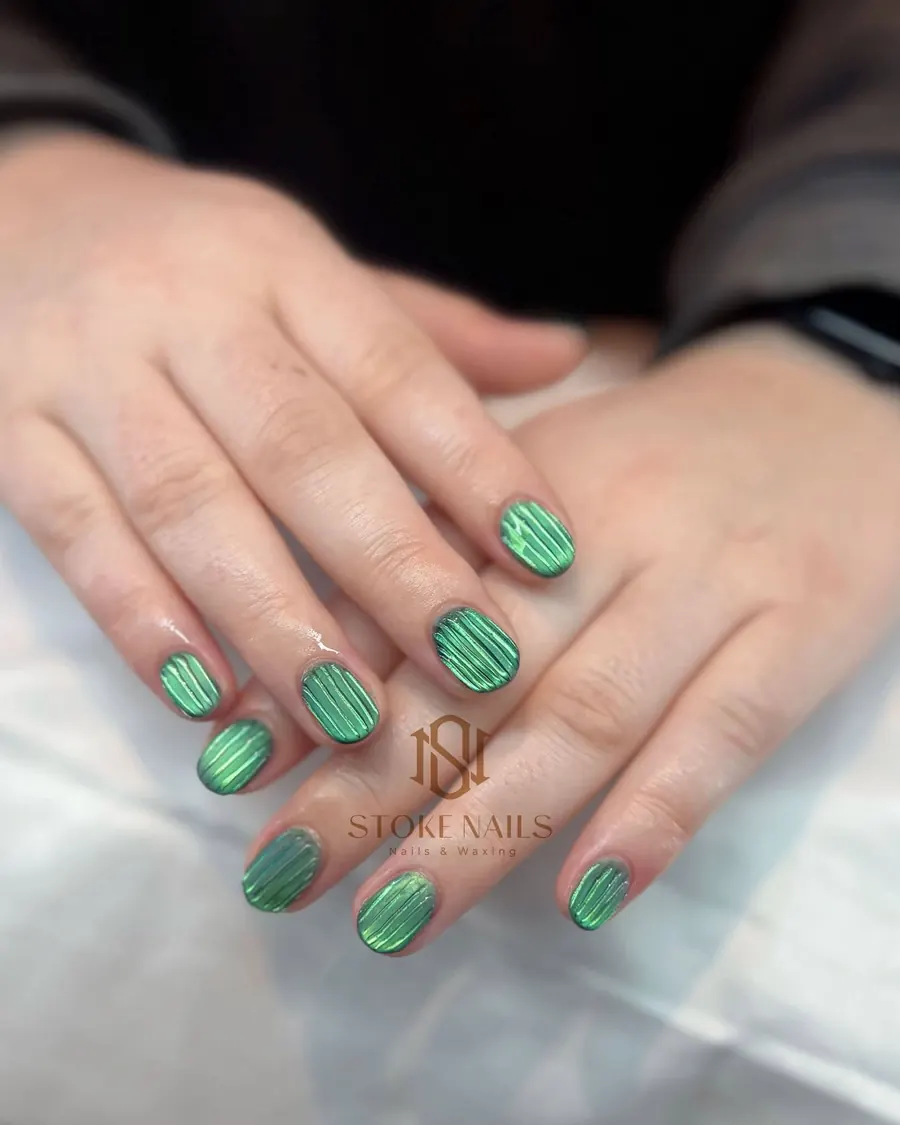 Short rounded nails in glossy green with fine vertical stripes